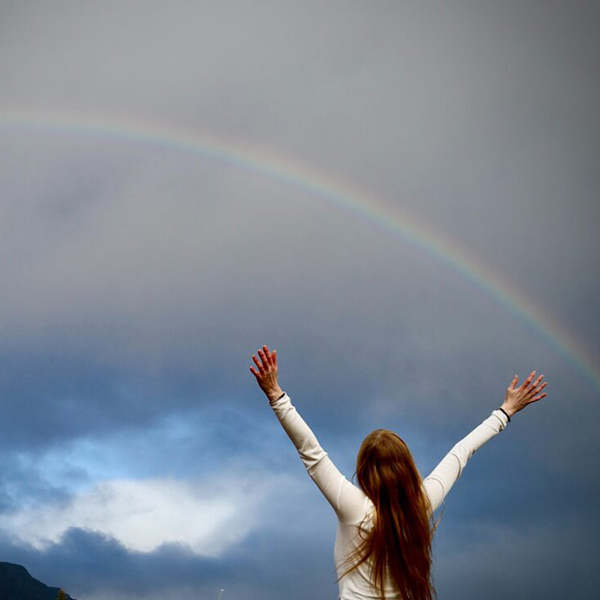 Ragazza che apre le mani al cielo con arcobaleno
