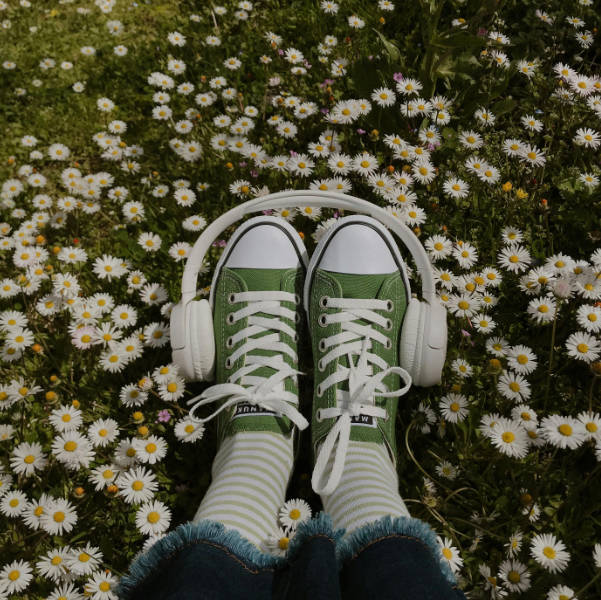 Scarpe verdi con cuffie audio su prato di margherite